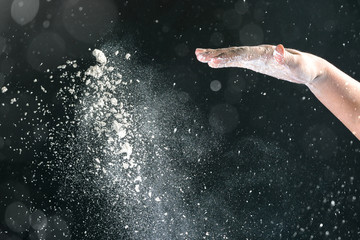 Fototapeta na wymiar Isolated on black background female hand pours white flour like snow for baking