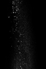 White powder in the form of snow or flour falls from top to bottom isolated on black background
