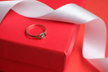 Wedding ring on a red gift box and a white ribbon.