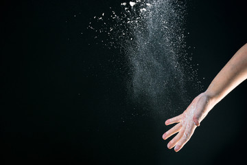 Hand of european woman chef in kitchen pouring flour on black background