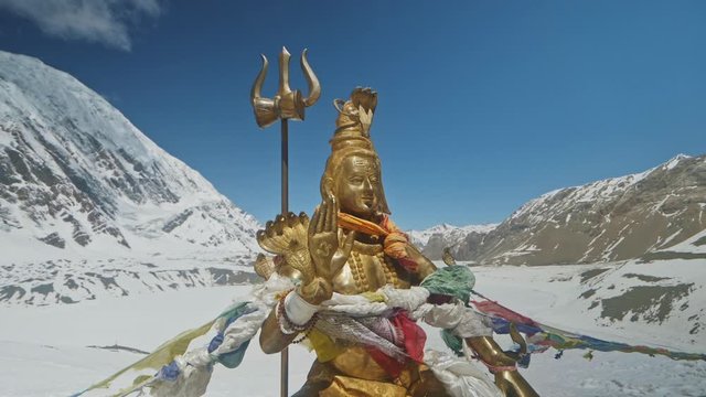 Golden statue of Lord Shiva shine at snowy Himalayas highlands against blue sky