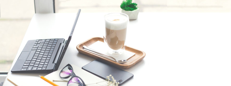 Desktop with laptop, smartphone, notepad and coffee maker.