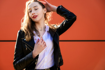 Naklejka premium Spring portrait of a smiling beautiful girl with emotions in the sun outdoors on an orange background. Model is wearing a white blouse and a jacket in front of the camera