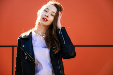 Spring portrait of a smiling beautiful girl with emotions in the sun outdoors on an orange background. Model is wearing a white blouse and a jacket in front of the camera