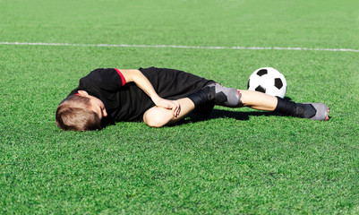 A young boy soccer player injured his leg during the match. Sufferer child football player and ball on the field. Kids injury in sport concept. Children's football school. Background. Copy space