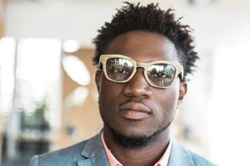 Serious trendy guy posing indoors. Closeup of young African American man wearing stylish glasses,...