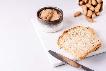 Homemade peanut paste or butter in a bowl and bread and peanuts on white marble tray. Healthy nutrition. Selective focus