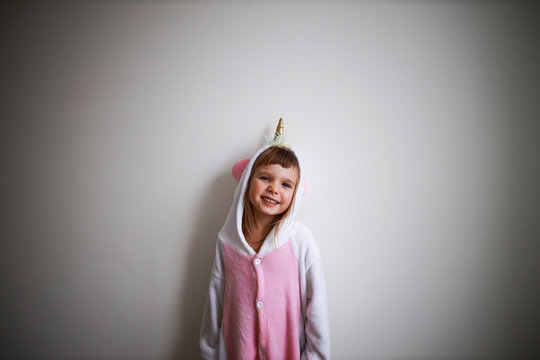portrait of little todder girl standing next to a white wall wearing unicorn kigurumi and looking at camera half-body portrait