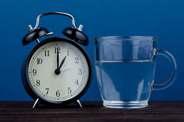 Alarm clock and a glass of water on a blue background. body water balance