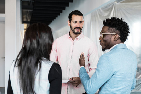 Interior designer meeting with customers and discussing renovation project. Young men and women in casual standing indoors, holding document, talking. Renovation concept