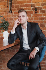 A handsome young bearded man blond in a suit and shirt in a restaurant with a loft interior. He sits at a table, read a magazine.