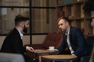 Two men in suits sit in a restaurant. A business meeting. Men drink coffee.