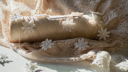 spool of thread with a needle, small white knitted flowers, delicate ivory lace