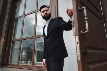 A young handsome man with a beard in a business suit stands on the street of the city.