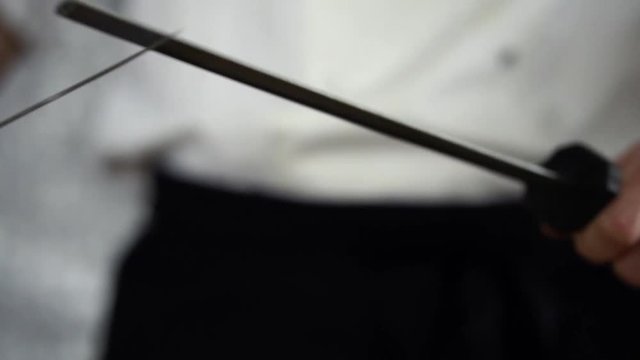 Chef in white uniform and black apron sharpening big Japanese knife with diamond covered steel stick