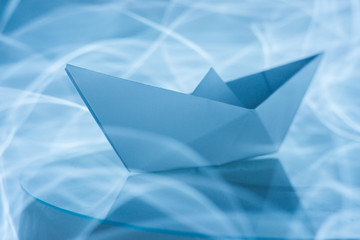 Paper boat splitting blue light trails symbolizing waves in the sea