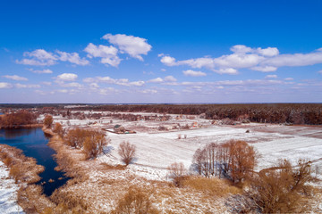 View from above of the countryside and brook on a sunny day. Snowy nature landscape with blue sky. Early spring