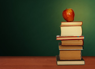 Back to school, pile of books and red apple with empty green school board background, education concept.