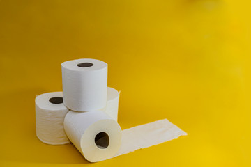 A stack of four white disposable toilet rolls on a bright yellow background. One roll lies untwisted. Soft fresh cotton. Essential goods. Purchasing power. Copy space. Side view.