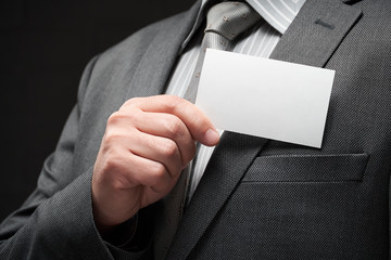 white blank business card closeup in businessman hand, gray suit, dark wall background