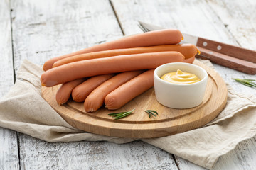 Raw frankfurter sausages with mustard on cutting board. - obrazy, fototapety, plakaty