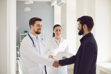 Handshake. Practicing doctor and patient shaking hands smiling at the clinic.