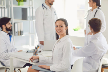 Obraz premium Female doctor sitting at a table with collegues in white lab coats at a medical hospital.