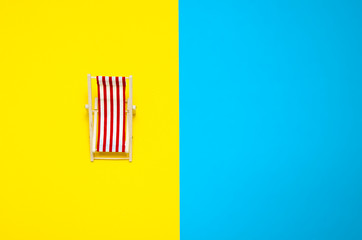 Miniature deck chair on yellow and blue background. Summer holidays concept. Summer concept.