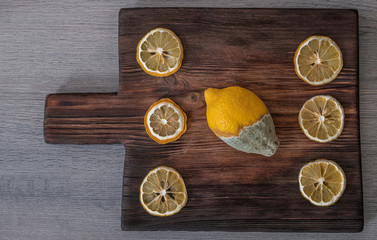 Old rotten lemon with dry slices on wooden board