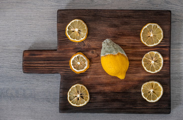 Old rotten lemon with dry slices on wooden board