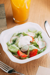 Restaurant serving salad with cheese, tomatoes and herbs. Fresh vegetable salad on a white plate.