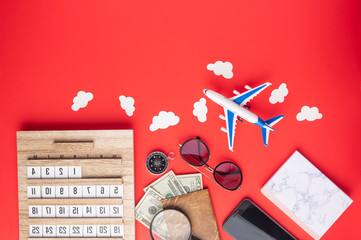 Sunny mood, time for travel and leisure, and planning. Against a red background, an airplane, a compass, sunglasses, a notebook and a phone. A schedule. With space for advertising for tour agencies.