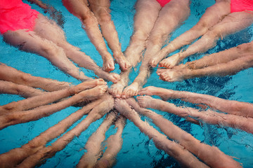 The legs of the synchronized swimmers girls peek out from the pool water and create the shape of a...