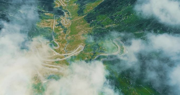Beautiful landscape view with mountains, road serpantine from above through white light clouds.