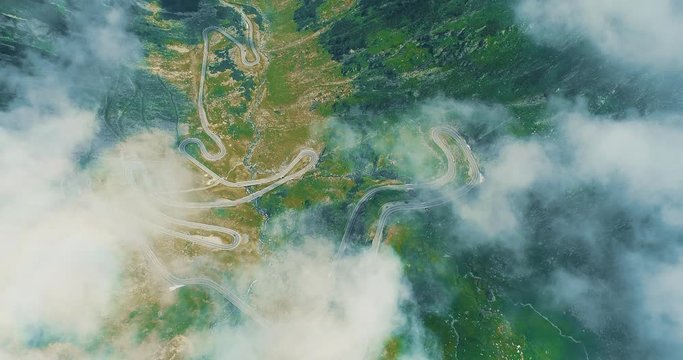 Beautiful landscape view with mountains, road serpantine from above through white light clouds.