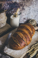 A sourdough bread  with wheat spikes aside and a container with flour behind it