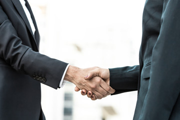 Female business partners meeting outside. Business women in office suits standing and shaking hands. Collaboration concept