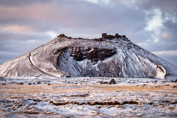 An old inactive volcano covered in snow, with a staircase leading to its peak and people climbing it on a cloudy winter day in Iceland