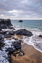 beach with cliff and stones on the shore of the Atlantic Ocean on a cloudy winter day in Iceland