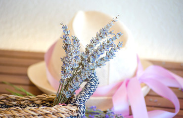 Light straw hat on a wooden brown table. Lilac-pink ribbon on the hat of a woman's hat. A bouquet of dry lavender in a rustic wicker straw basket.