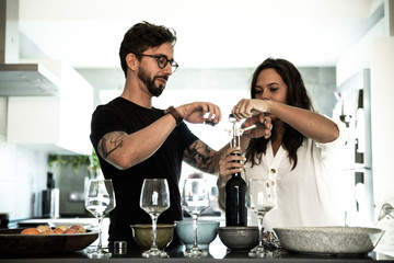 Sweet couple celebrating anniversary and opening wine bottle together in kitchen. Young man and woman in casual meeting indoors. Dinner at home concept