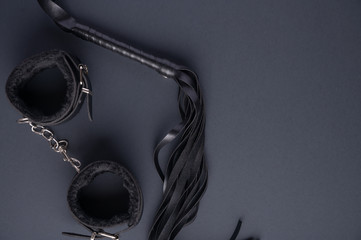 Accessories for bdsm on a black background. Leather lash and leather handcuffs. Valentine's Day. Erotic shop. Copy space