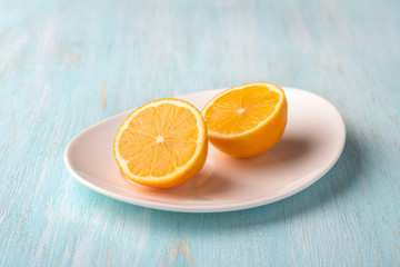 White plate with a cutted on two halfs ​​organic lemon on a blue background, selective focus, space