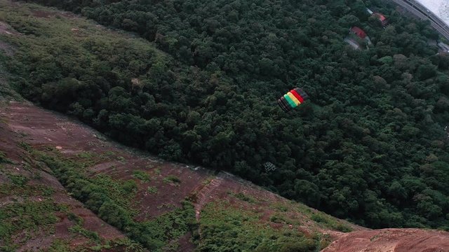 Aerial View Of Parachuter Gliding Down Past Large Cliff Face And Over Lush Green Forest