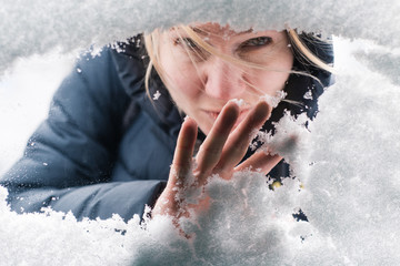 A young girl looks out the window and with her hand cleans the frozen glass from snow. Help and...