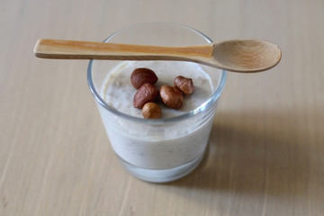Glass of vanilla pudding with hazelnut topping and wooden spoon. Selective focus.
