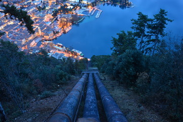 Pipes hydroelectric power station, at night with vegetation and illuminated city viewed from above,...