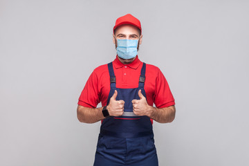 Work are done! Portrait of young man with surgical medical mask in blue overall, red t-shirt , cap,...
