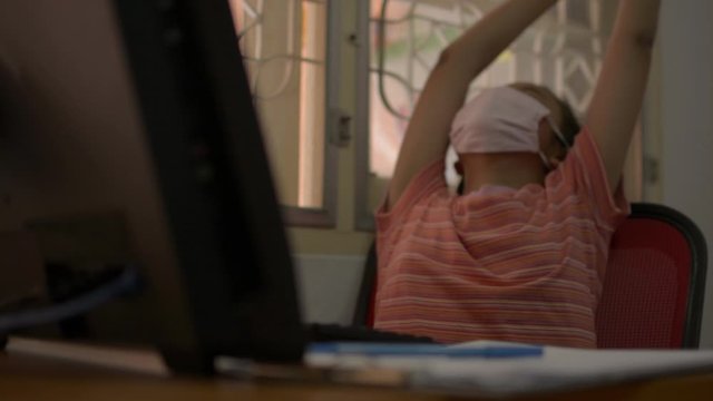 Cute girl wearing protective mask working with computer on the desk and stretch herself for stress relief at home during COVID-19 outbreak situation. Study at home concept.