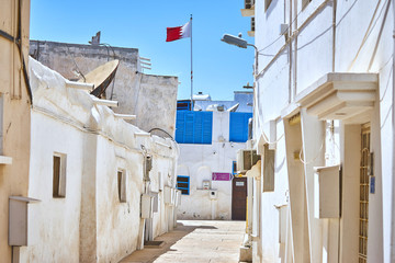 Narrow quiet arabian street in the old district of Bahrain with a national flag
